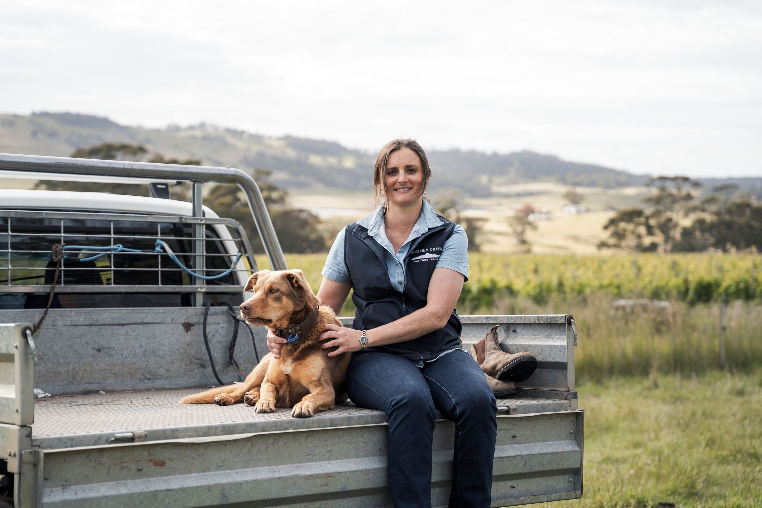 Astrid Maurits and Spud the sheep herding dog on a ute tray at Boomer Creek Vineyard, Little Swanport