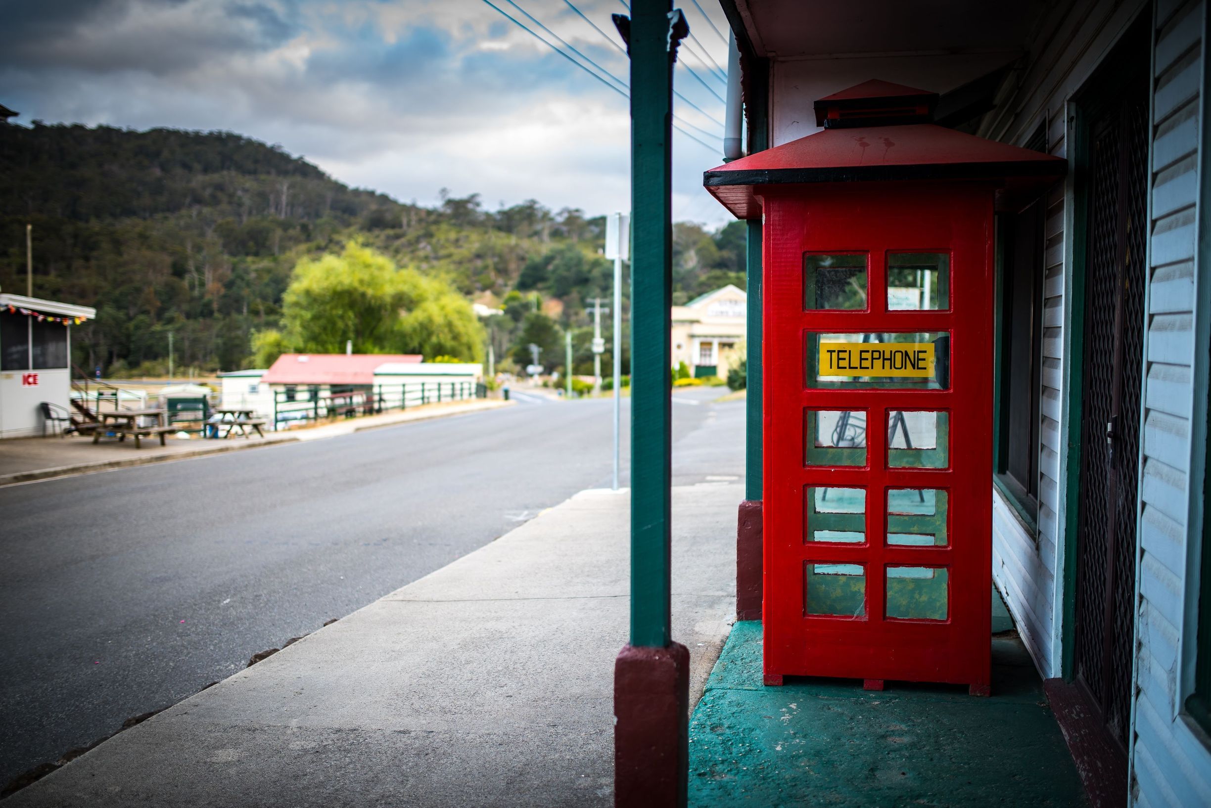 Derby streetscape with a red telephone box on a quiet footpath, weatherboard buildings and forested hills beyond