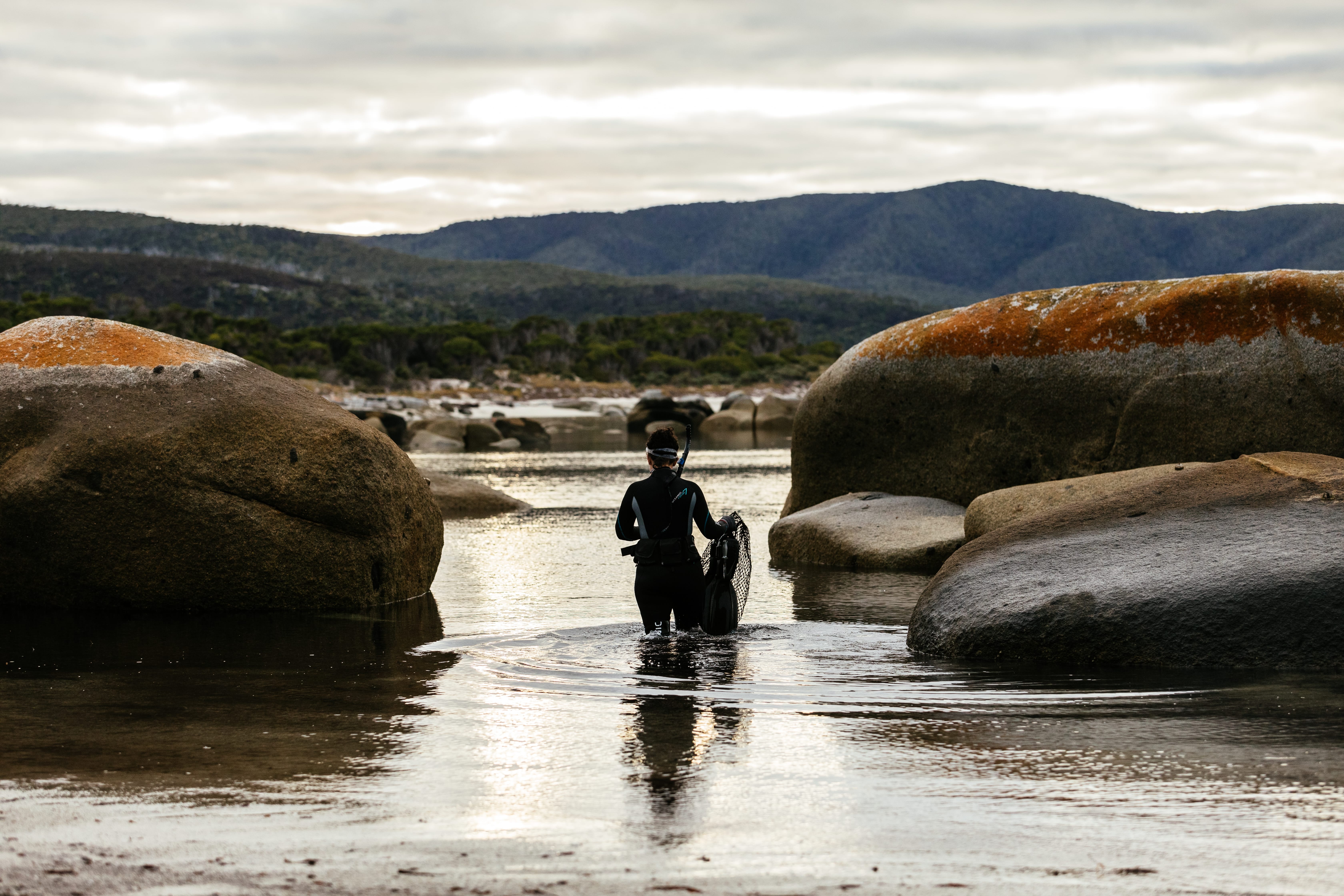 A snorkeller wading between granite boulders with snorkel and net on Flinders Island, Tasmania