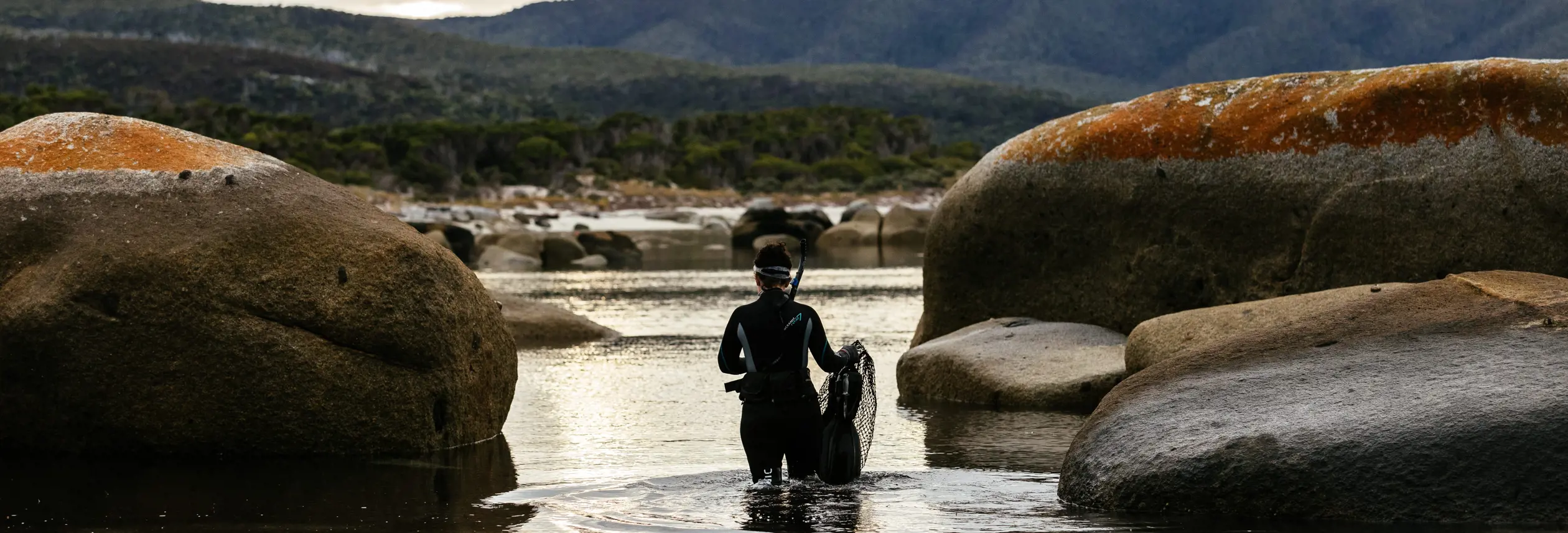 A snorkeller wading between granite boulders with snorkel and net on Flinders Island, Tasmania