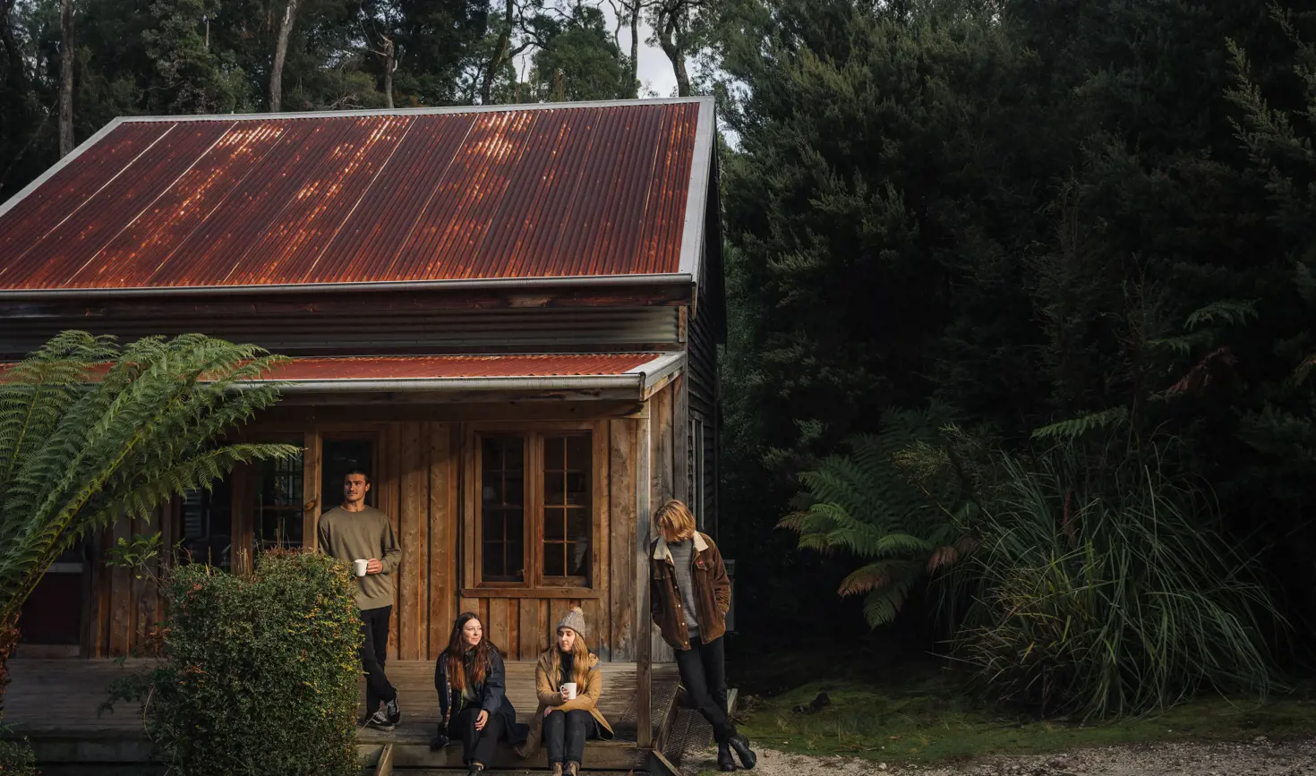 Guests on the porch of a timber miners cottage at Corinna Wilderness Village, takayna / Tarkine, Tasmania's West Coast