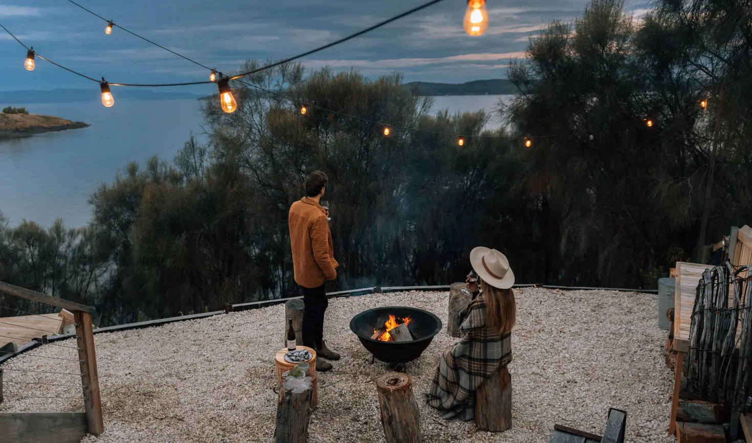 Guests by a firepit and string lights with ocean views at Driftwood Cabin, Primrose Sands, Tasmania