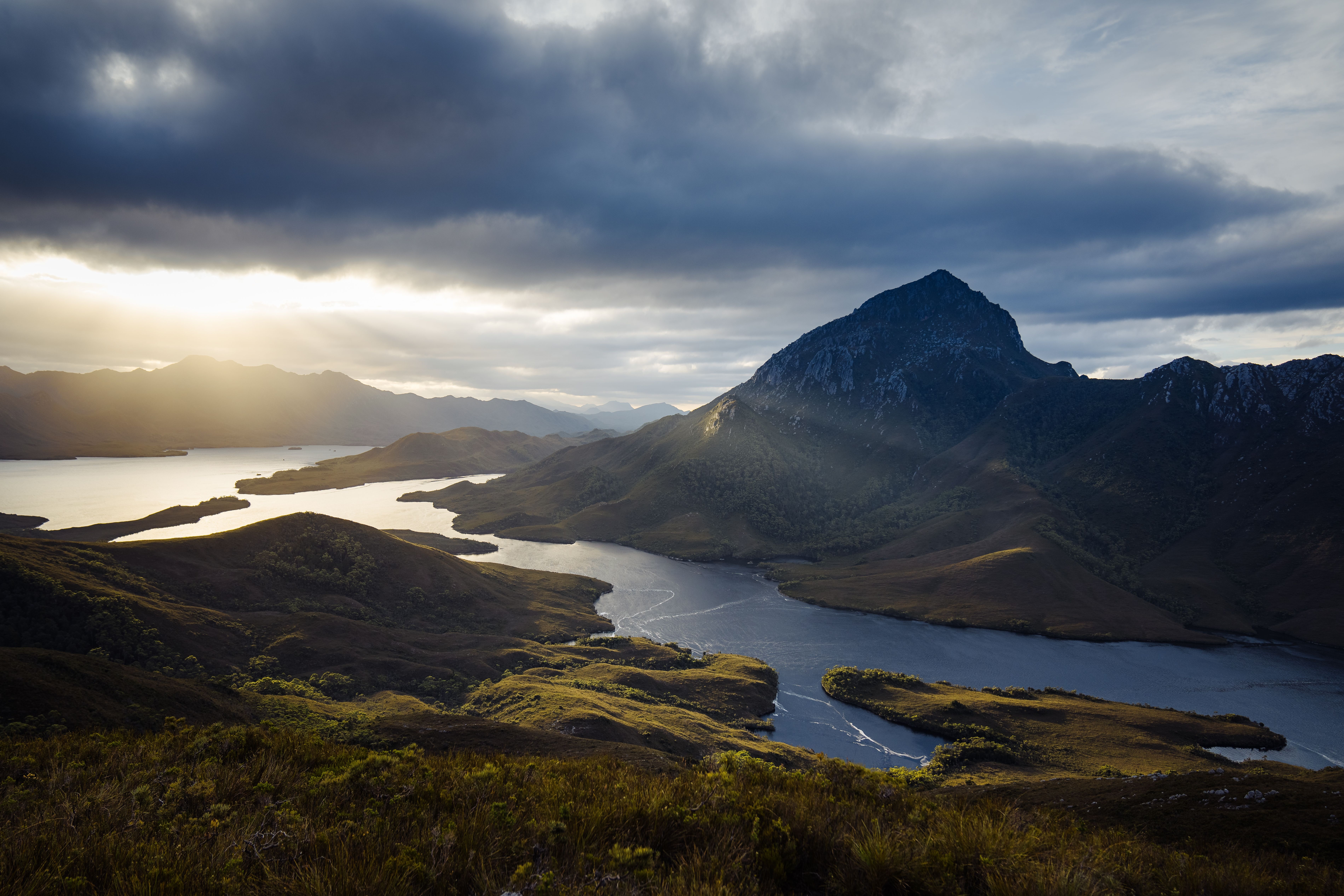 Sunlight breaking through clouds over Bathurst Harbour and surrounding mountains, Southwest National Park Tasmania