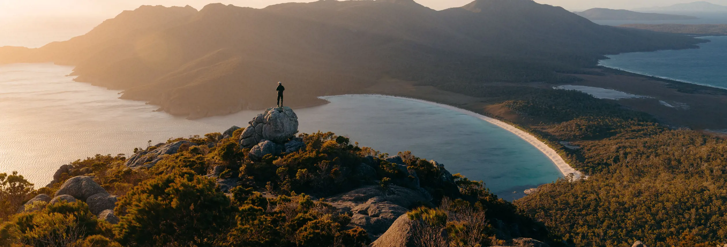 Person on a granite outcrop overlooking Wineglass Bay, Freycinet National Park, Tasmania