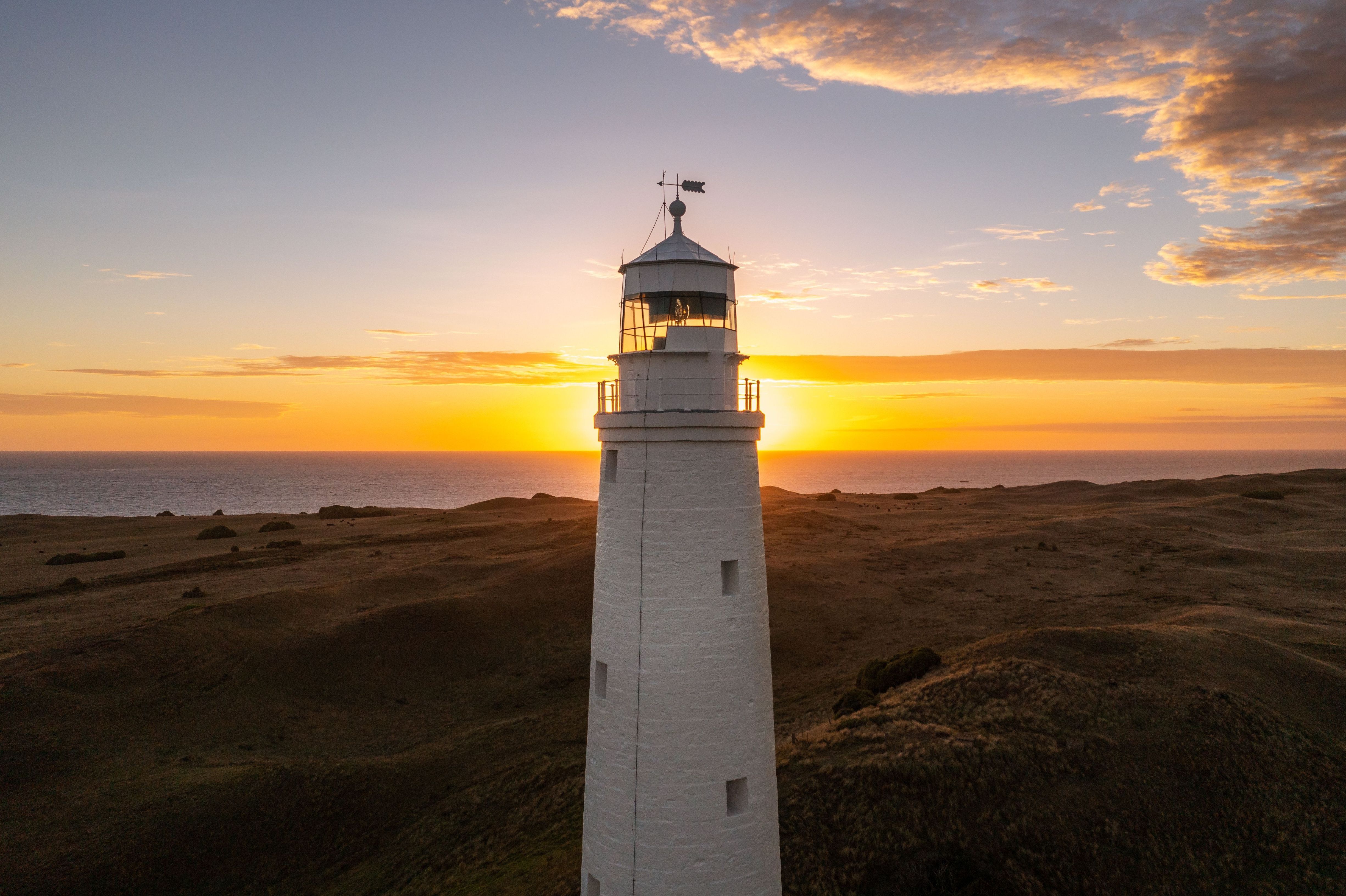 Cape Wickham Lighthouse with the sun on the horizon over the sea, King Island, Tasmania