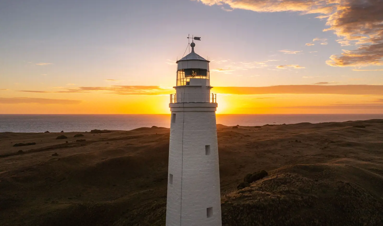 Cape Wickham Lighthouse with the sun on the horizon over the sea, King Island, Tasmania