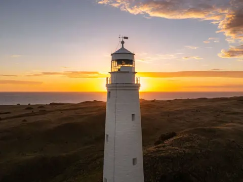 Cape Wickham Lighthouse with the sun on the horizon over the sea, King Island, Tasmania