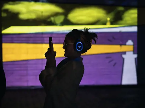 A visitor with headphones taking a photo at the immersive Permission to Trespass event in ArtsCape, Wynyard, Tasmania