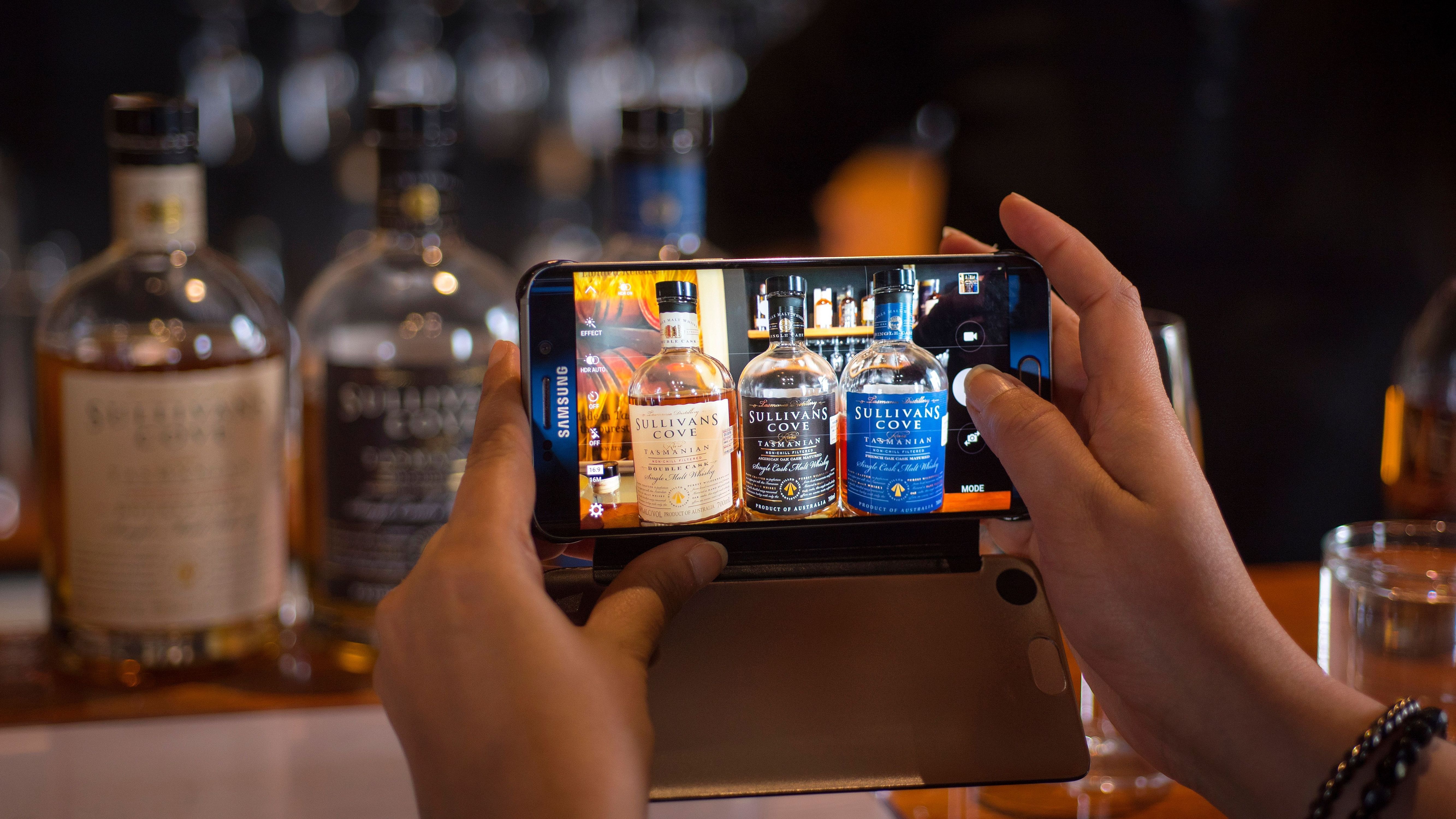 Hands holding a phone photographing Tasmanian whisky bottles including Sullivans Cove, Hobart, Tasmania