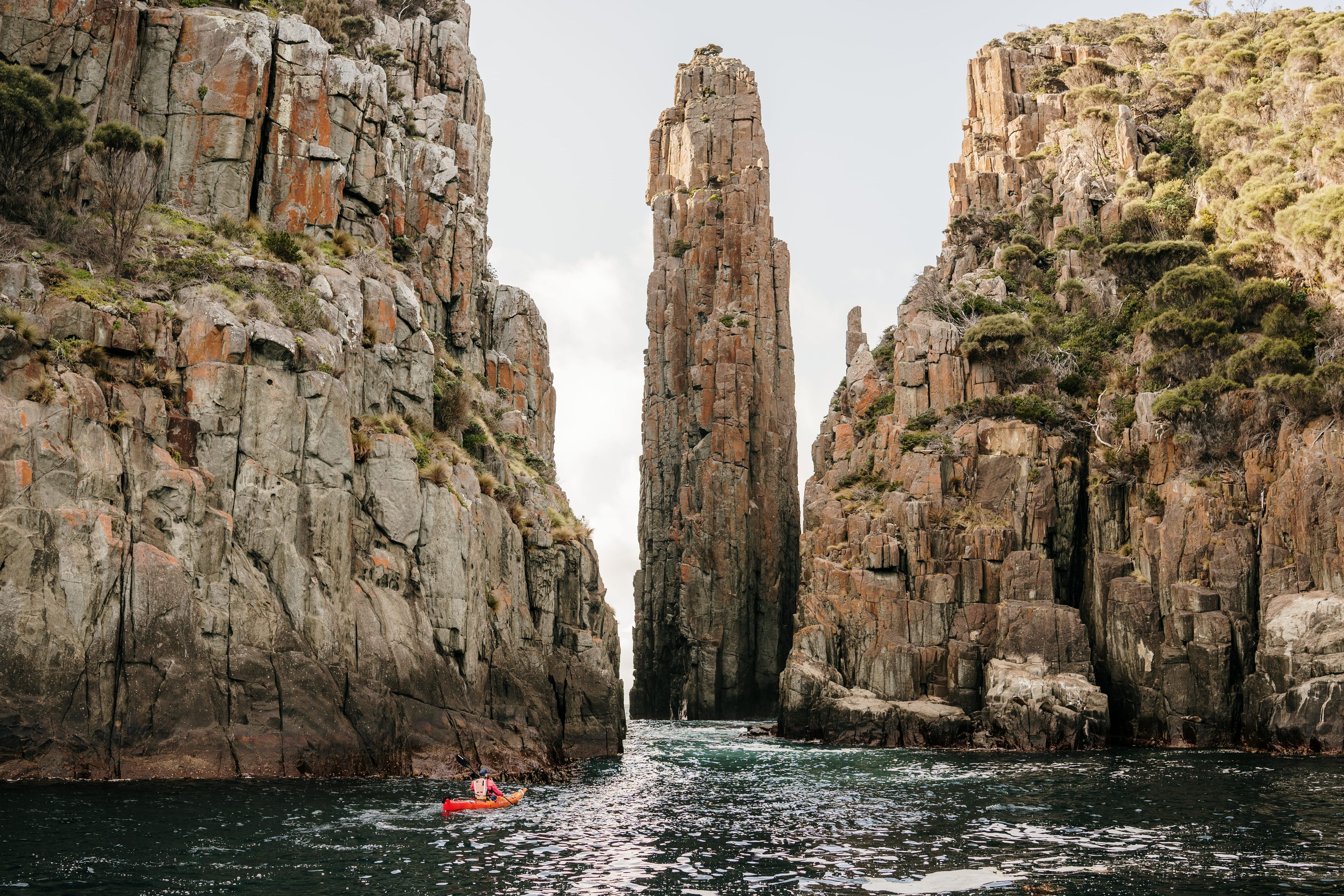 A kayaker dwarfed by towering rock columns with Southern Sea Ventures, Turrakana / Tasman Peninsula, Tasmania