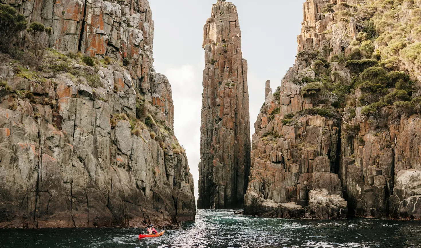 A kayaker dwarfed by towering rock columns with Southern Sea Ventures, Turrakana / Tasman Peninsula, Tasmania