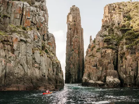 A kayaker dwarfed by towering rock columns with Southern Sea Ventures, Turrakana / Tasman Peninsula, Tasmania