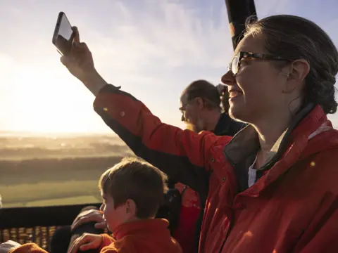Passengers in a hot air balloon basket with one taking a photo on a phone, Launceston, Tasmania