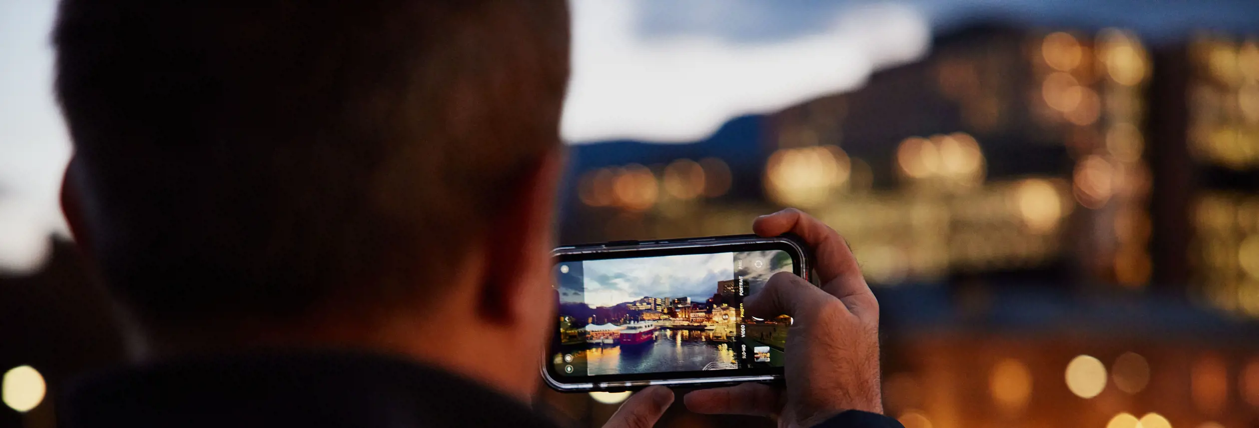 A photographer capturing the Hobart waterfront at twilight on a phone, Hobart, Tasmania