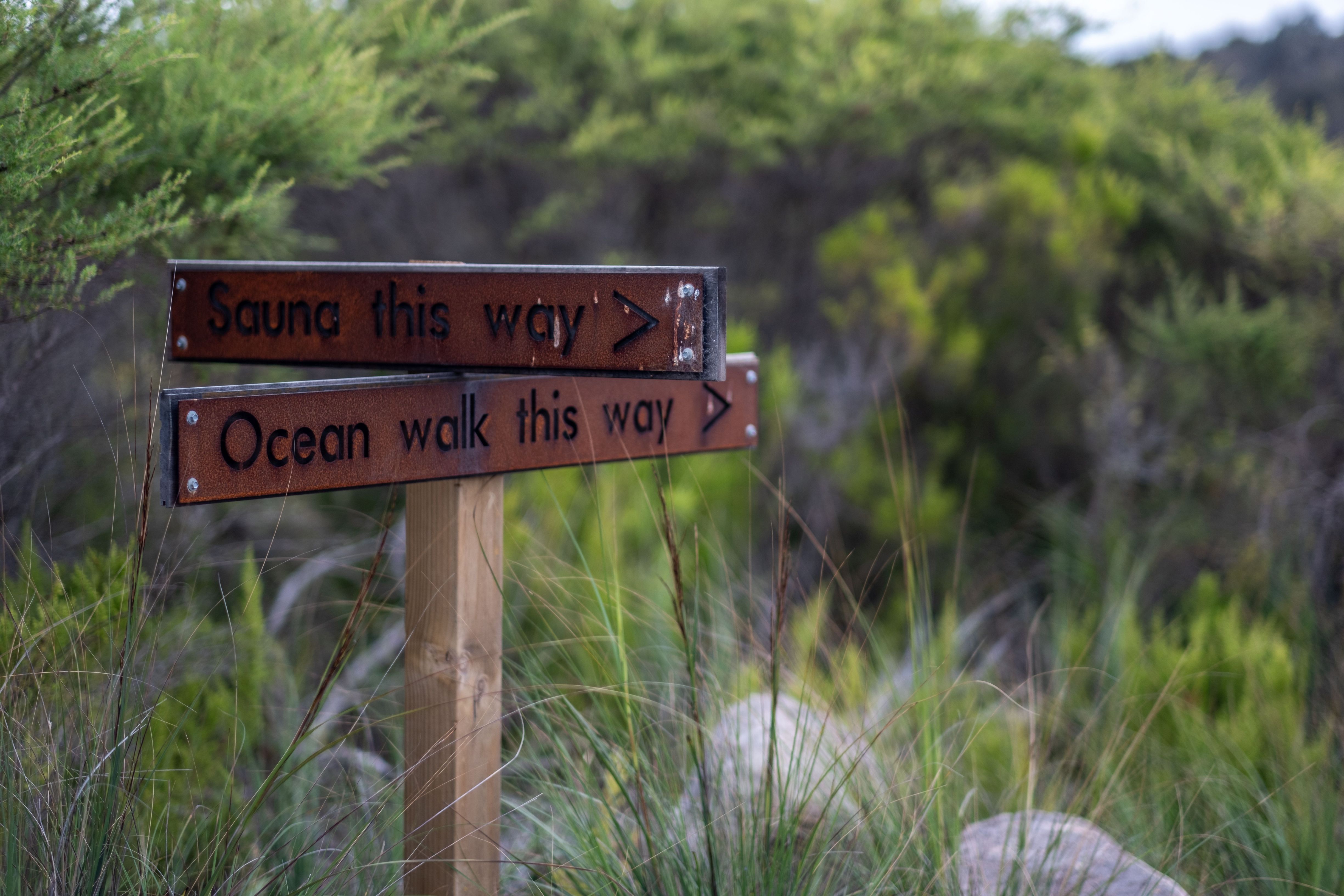Wooden directional signs reading "Sauna this way" and "Ocean walk this way" at Little Beach Co. Resort, Chain of Lagoons, Tasmania