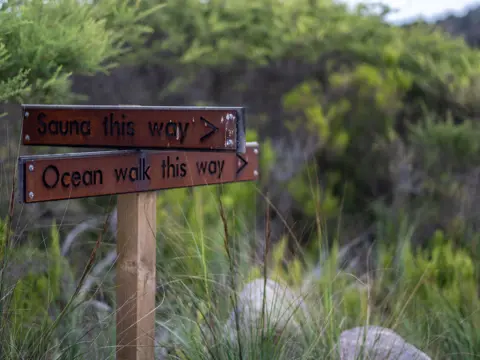 Wooden directional signs reading "Sauna this way" and "Ocean walk this way" at Little Beach Co. Resort, Chain of Lagoons, Tasmania