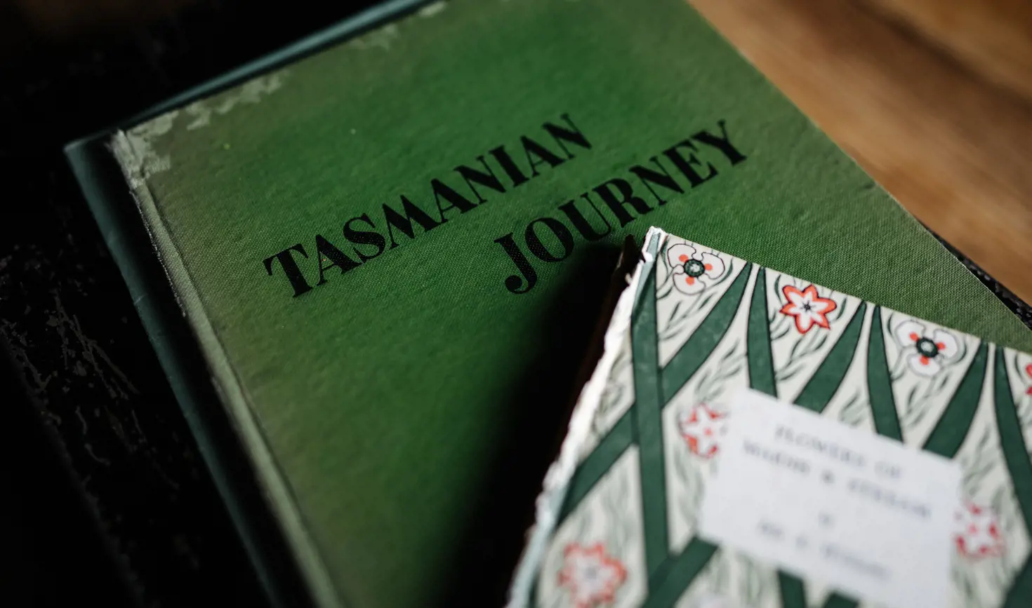 A vintage book titled "Tasmanian Journey" beside a book with a decorative floral cover
