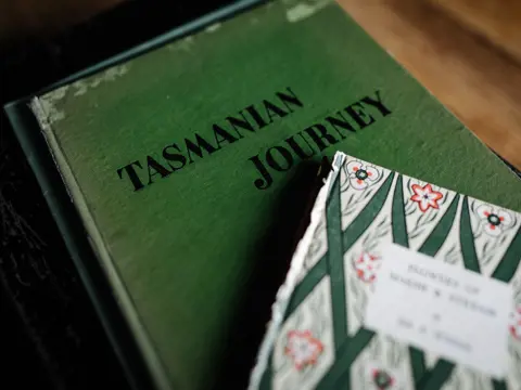 A vintage book titled "Tasmanian Journey" beside a book with a decorative floral cover