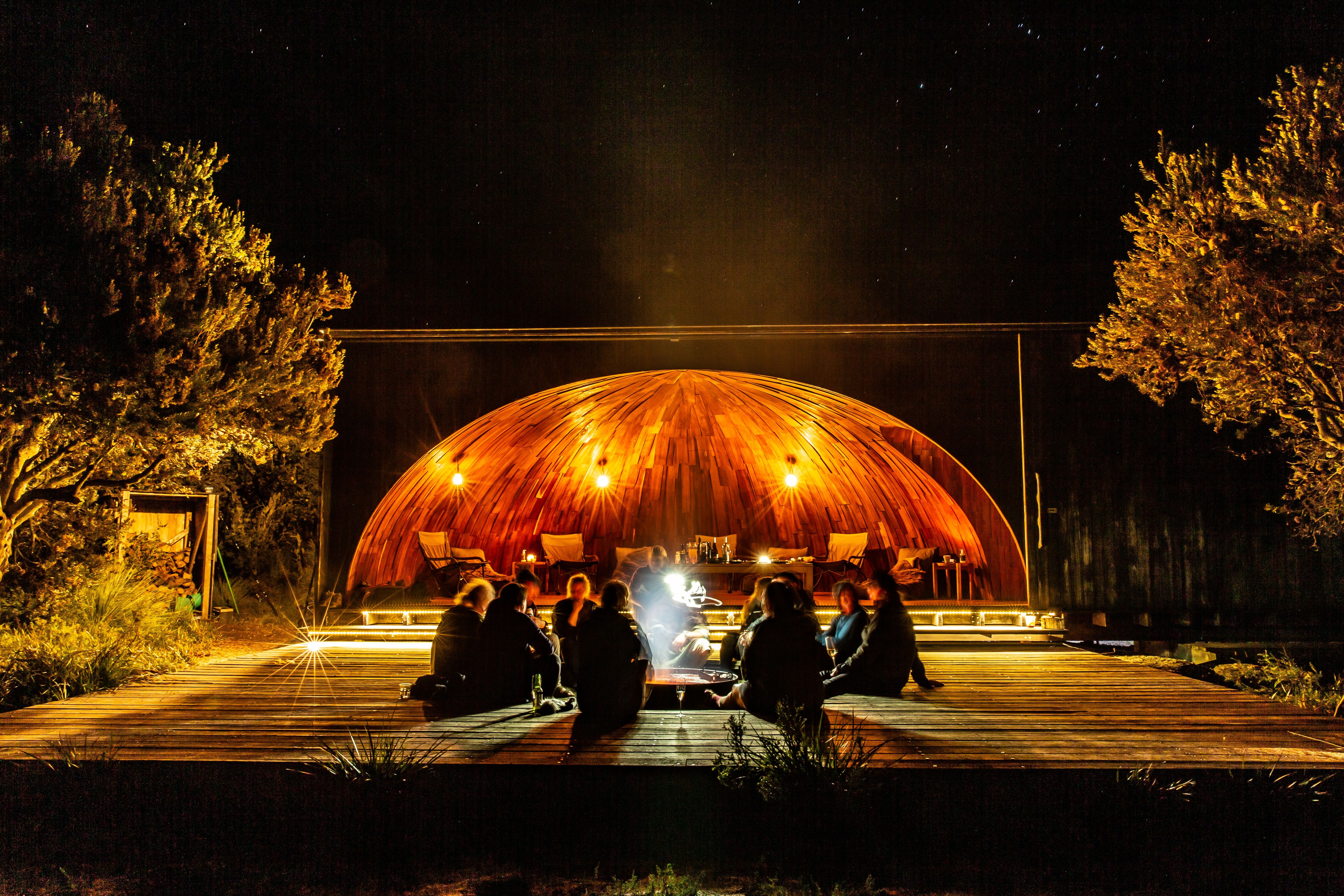 People sitting around an open fire at krakani lumi standing camp on wukalina Walk, wukalina / Mount William National Park