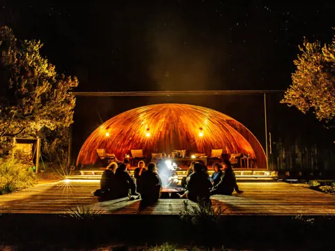 People sitting around an open fire at krakani lumi standing camp on wukalina Walk, wukalina / Mount William National Park