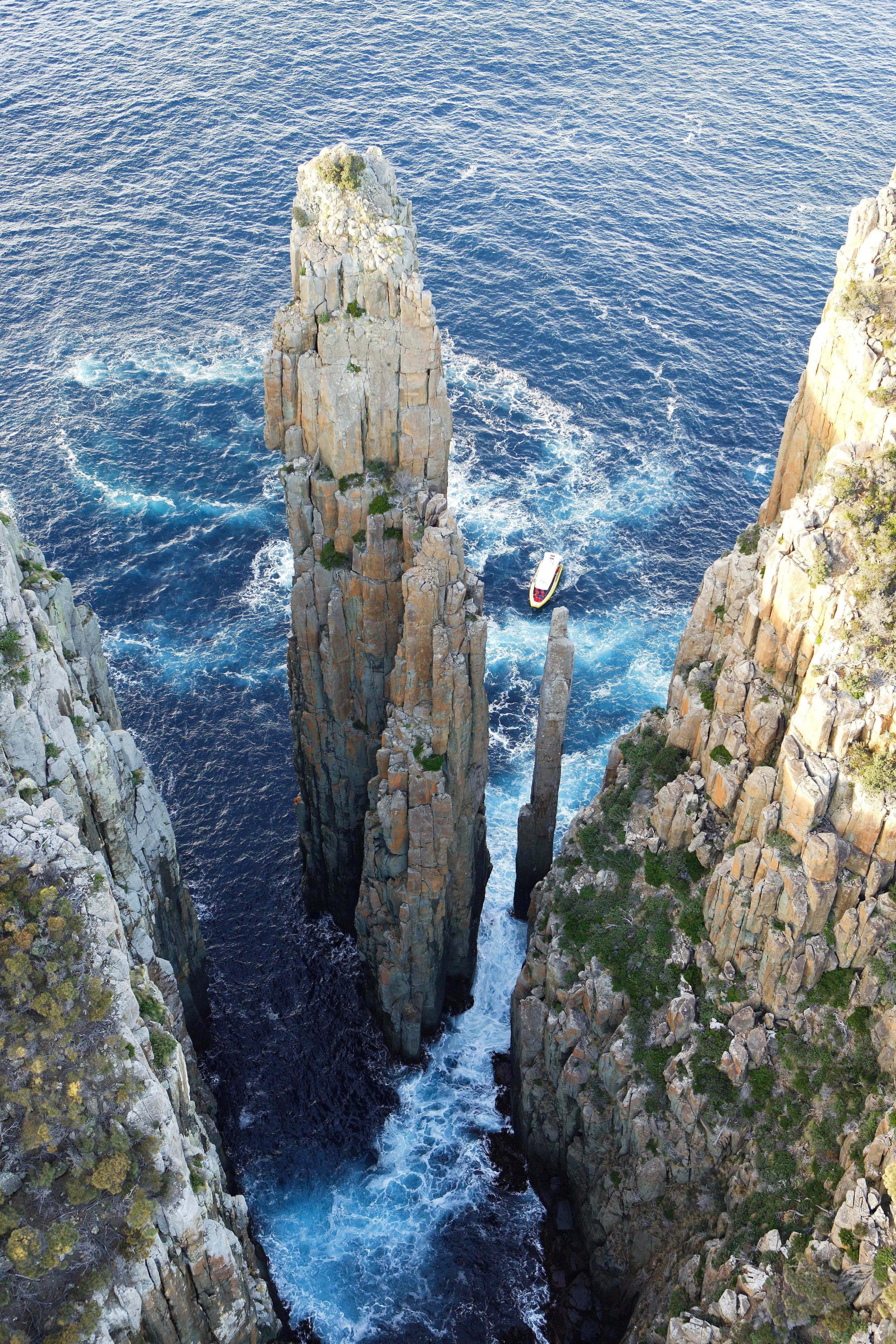 Aerial view of a Tasman Island Cruises boat passing The Candlestick and the Totem Pole sea stacks at Cape Hauy, Turrakana / Tasman Peninsula, Tasmania