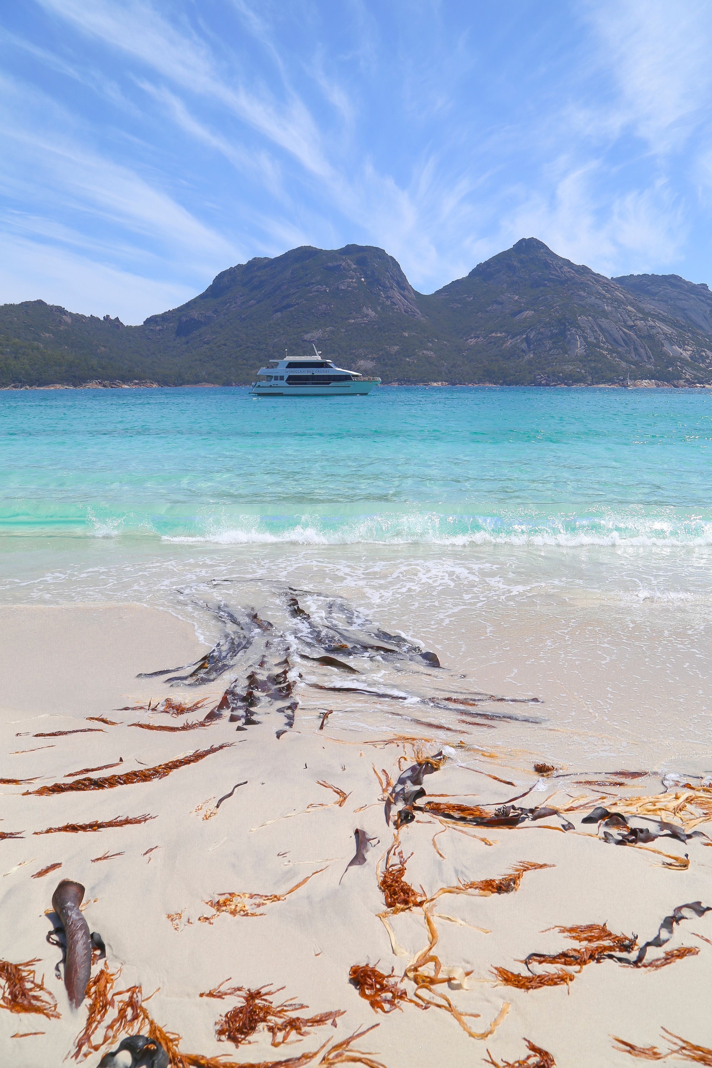 Wineglass Bay Cruises boat anchored in turquoise water with The Hazards mountains in the background, Wineglass Bay, Freycinet National Park, Tasmania