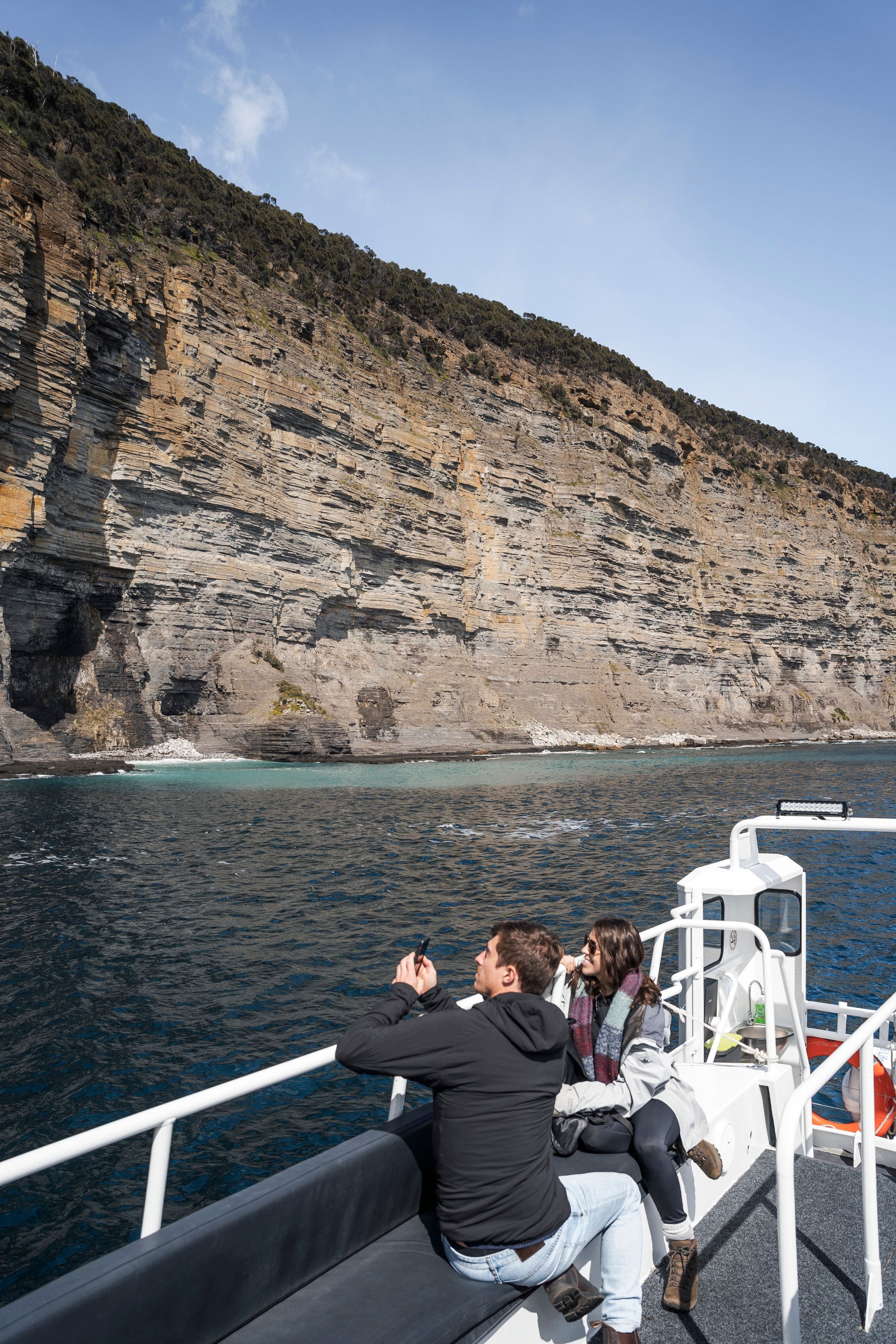 Two passengers photographing dolerite sea cliffs from the deck of a Maria Island Cruises boat, Tasmania