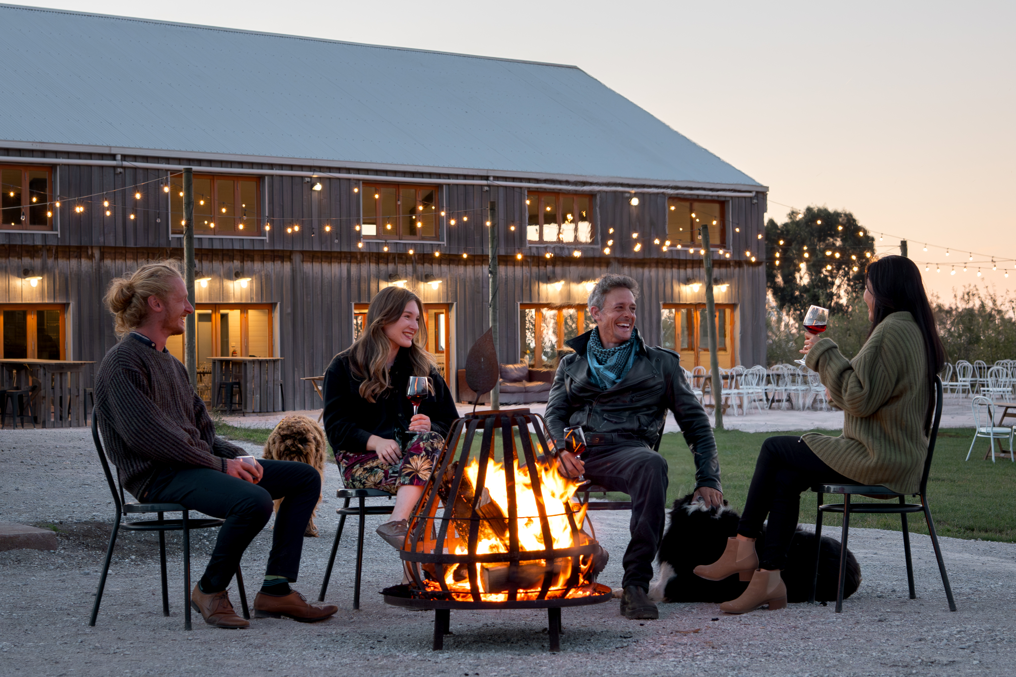 Guests gathered around a fire pit with wine and dogs outside the barn at Mount Gnomon Farm at dusk, Penguin, Tasmania