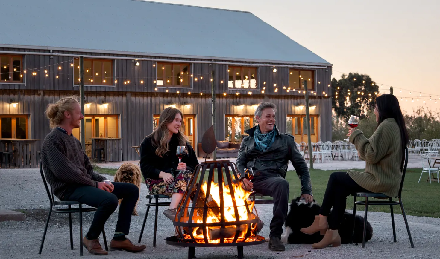 Guests gathered around a fire pit with wine and dogs outside the barn at Mount Gnomon Farm at dusk, Penguin, Tasmania