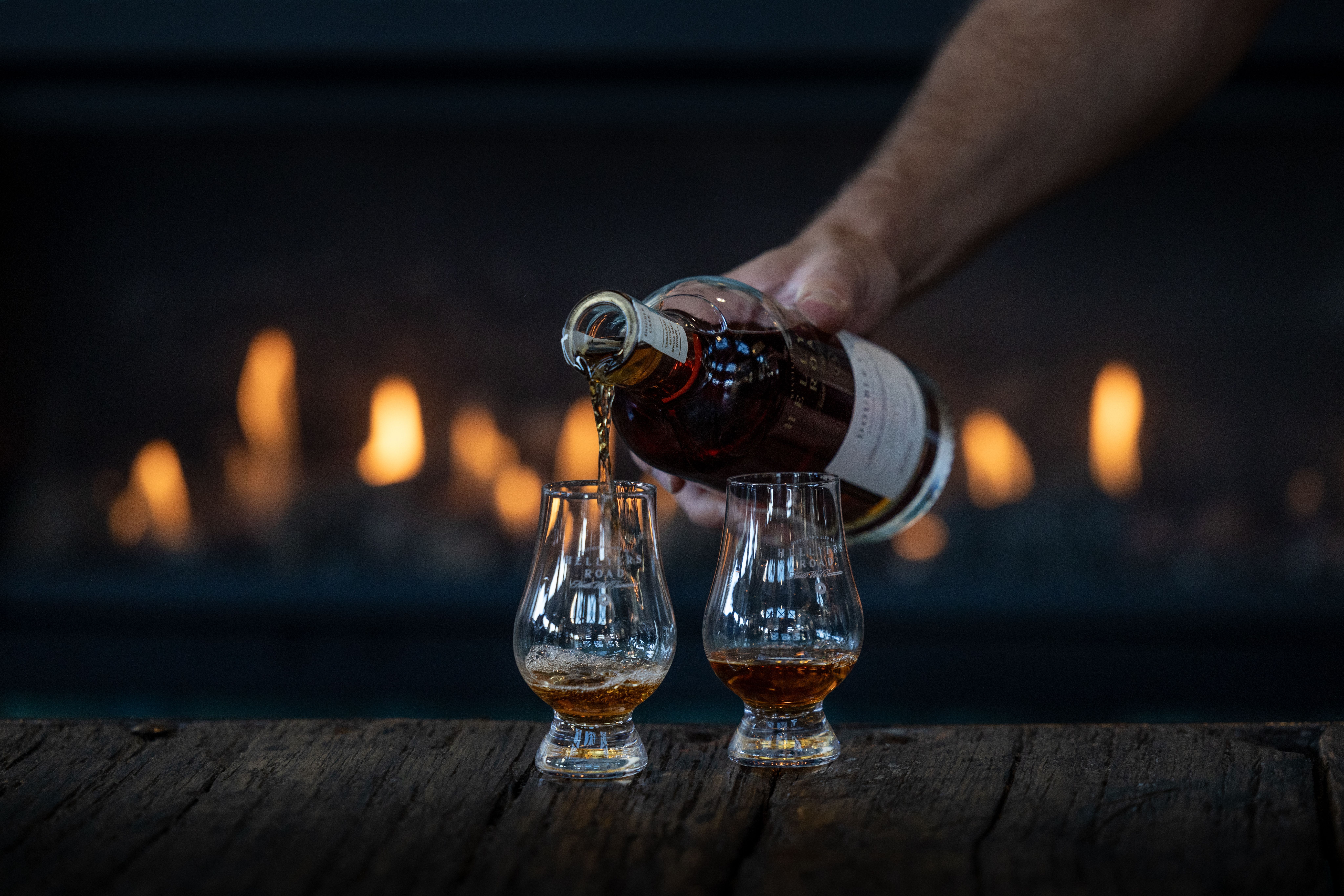 Hellyers Road Distillery whisky being poured into two tasting glasses in front of an open fire, Havenview, Tasmania