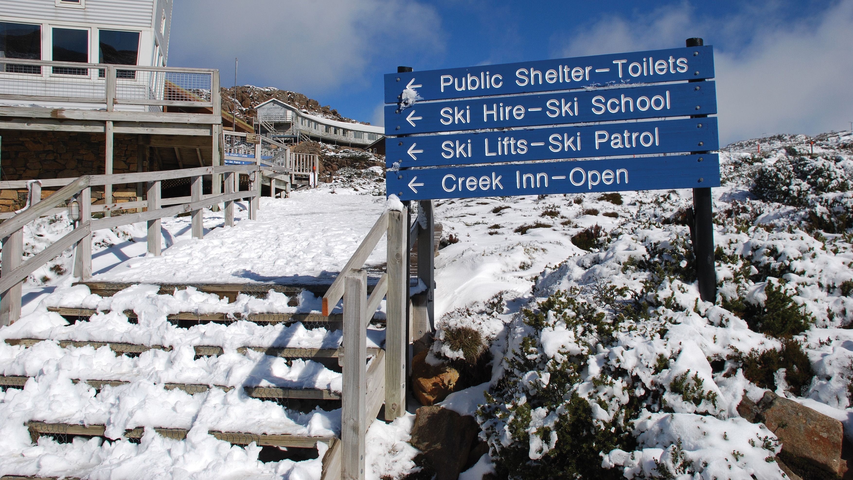 Snow-covered timber steps and blue directional signage for ski facilities and Creek Inn at Ben Lomond National Park