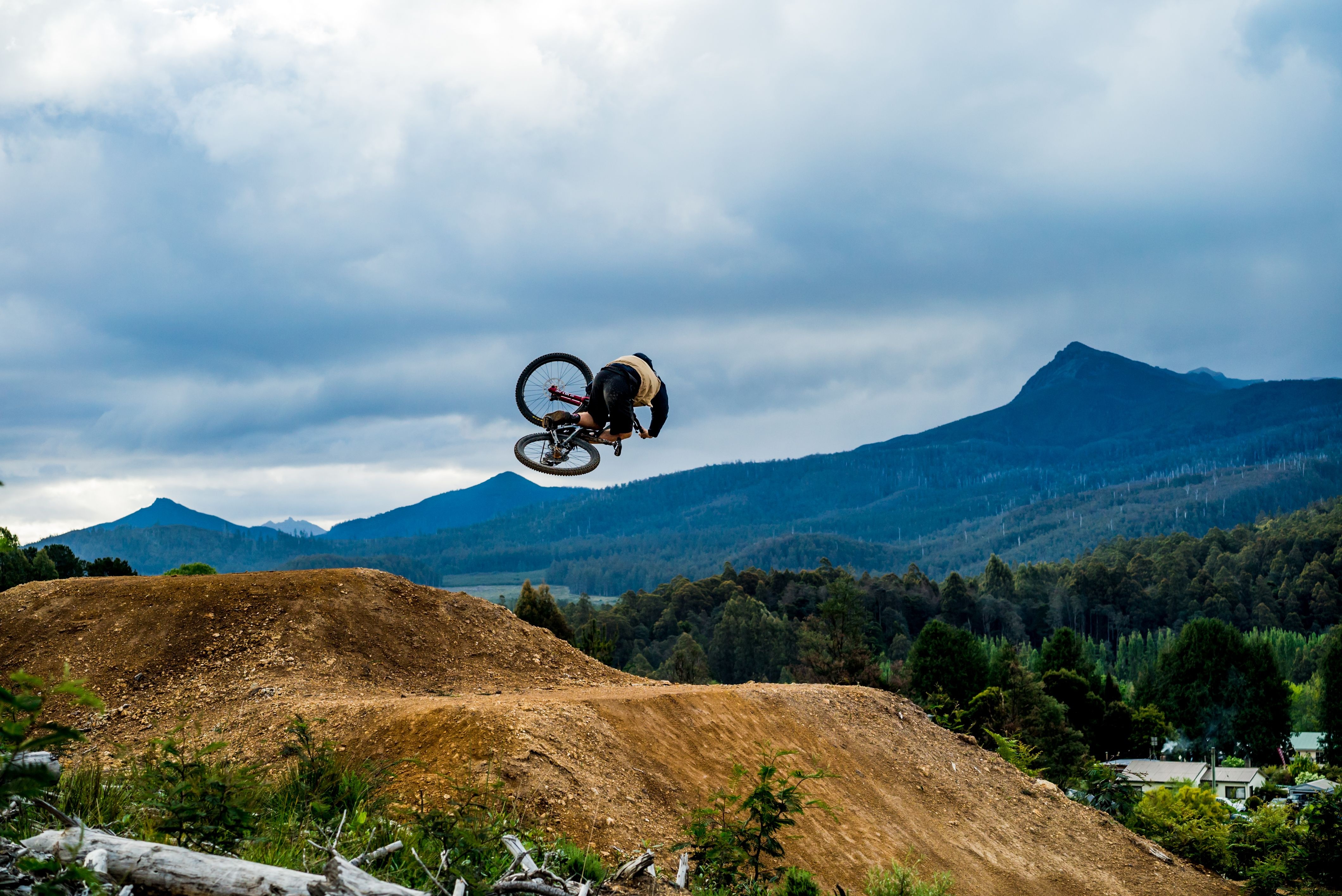 A mountain biker mid-jump on a dirt track with mountains behind at Maydena Bike Park, Derwent Valley, Tasmania