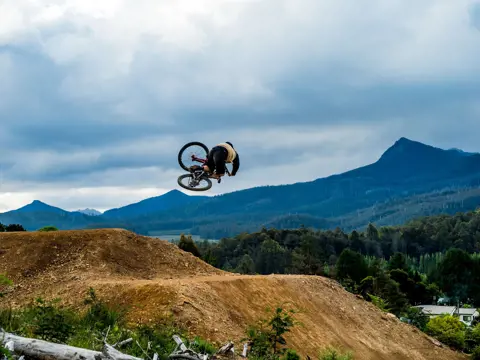 A mountain biker mid-jump on a dirt track with mountains behind at Maydena Bike Park, Derwent Valley, Tasmania