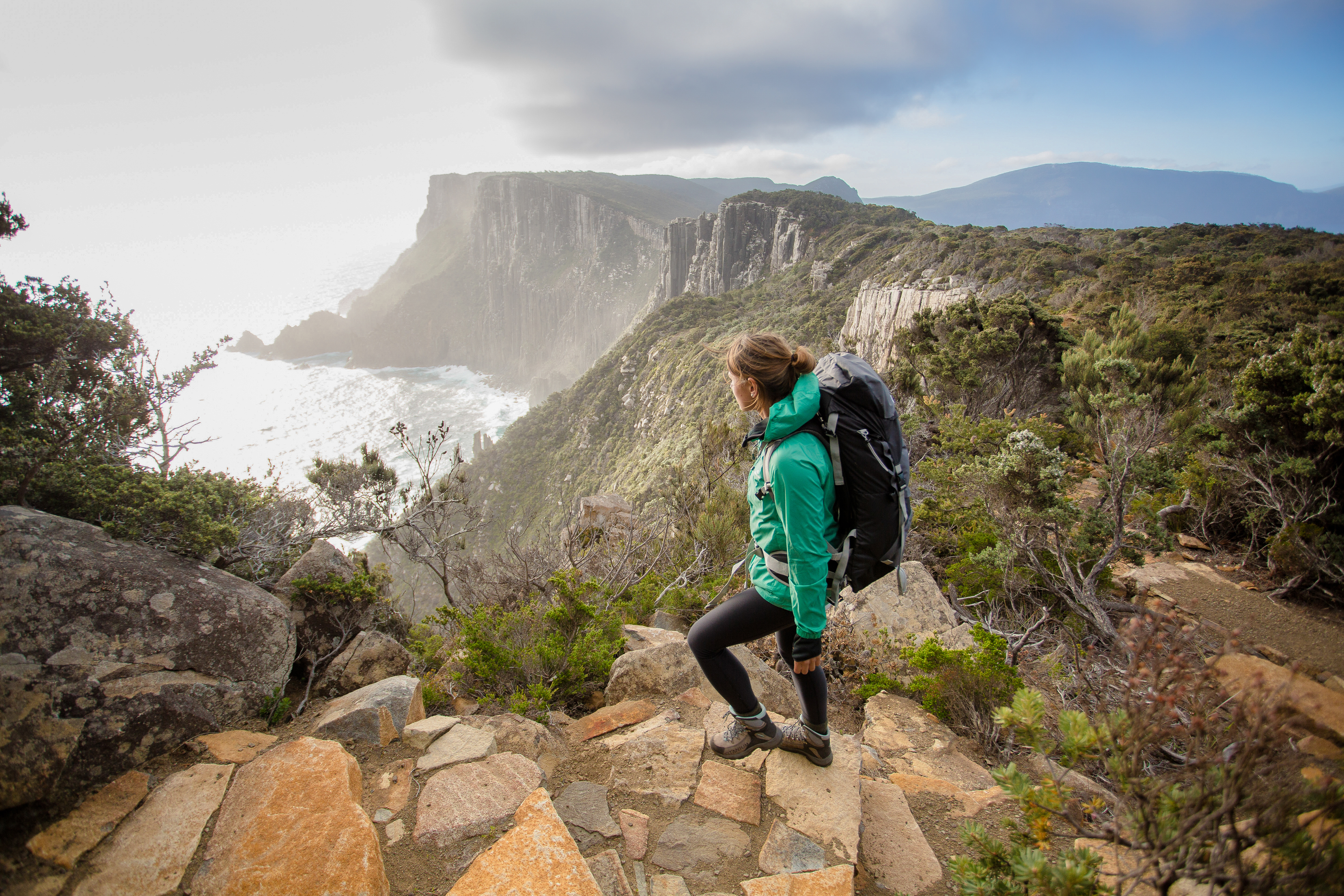 A walker on a rocky path looking out over Cape Pillar and The Blade, Three Capes Track, Turrakana / Tasman Peninsula