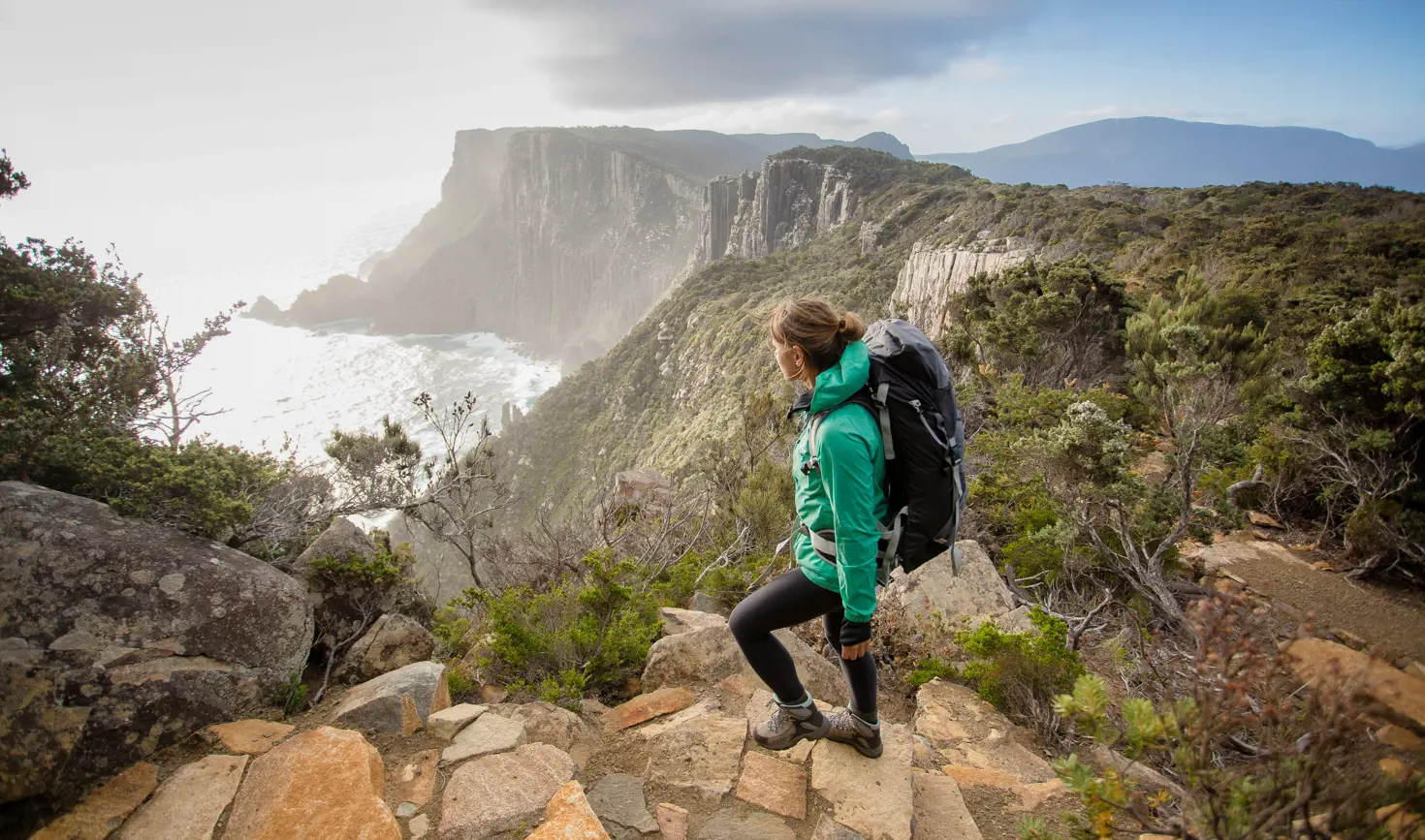 A walker on a rocky path looking out over Cape Pillar and The Blade, Three Capes Track, Turrakana / Tasman Peninsula