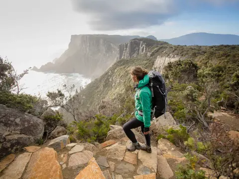A walker on a rocky path looking out over Cape Pillar and The Blade, Three Capes Track, Turrakana / Tasman Peninsula