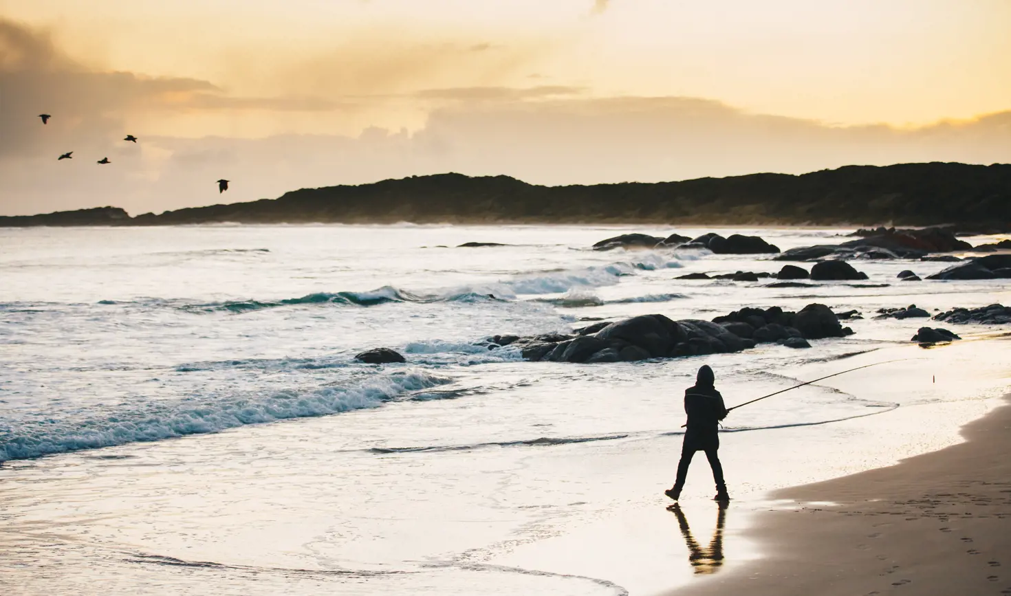 A silhouette of a person fishing on the beach in golden light, Disappointment Bay, King Island, Tasmania