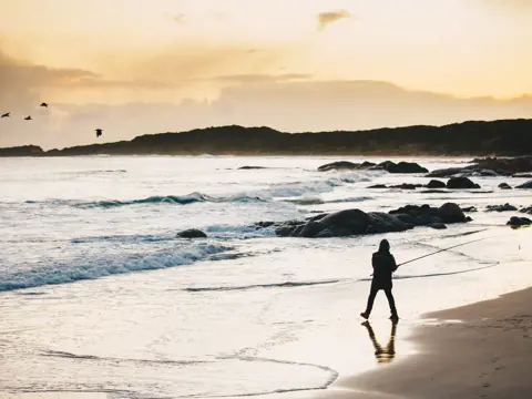 A silhouette of a person fishing on the beach in golden light, Disappointment Bay, King Island, Tasmania