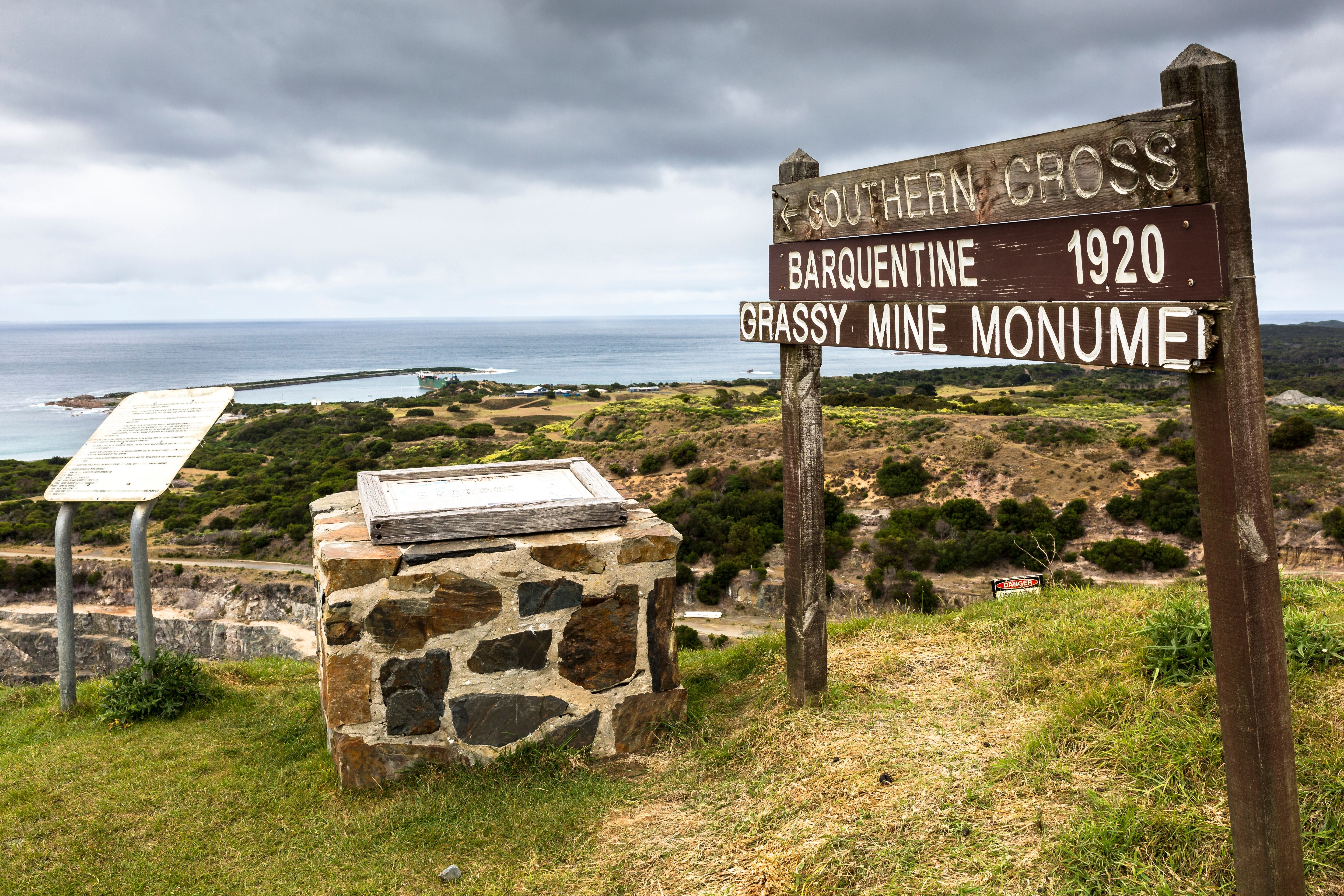 Wooden directional sign and stone monument at Grassy Mine Monument lookout overlooking the coast, King Island, Tasmania