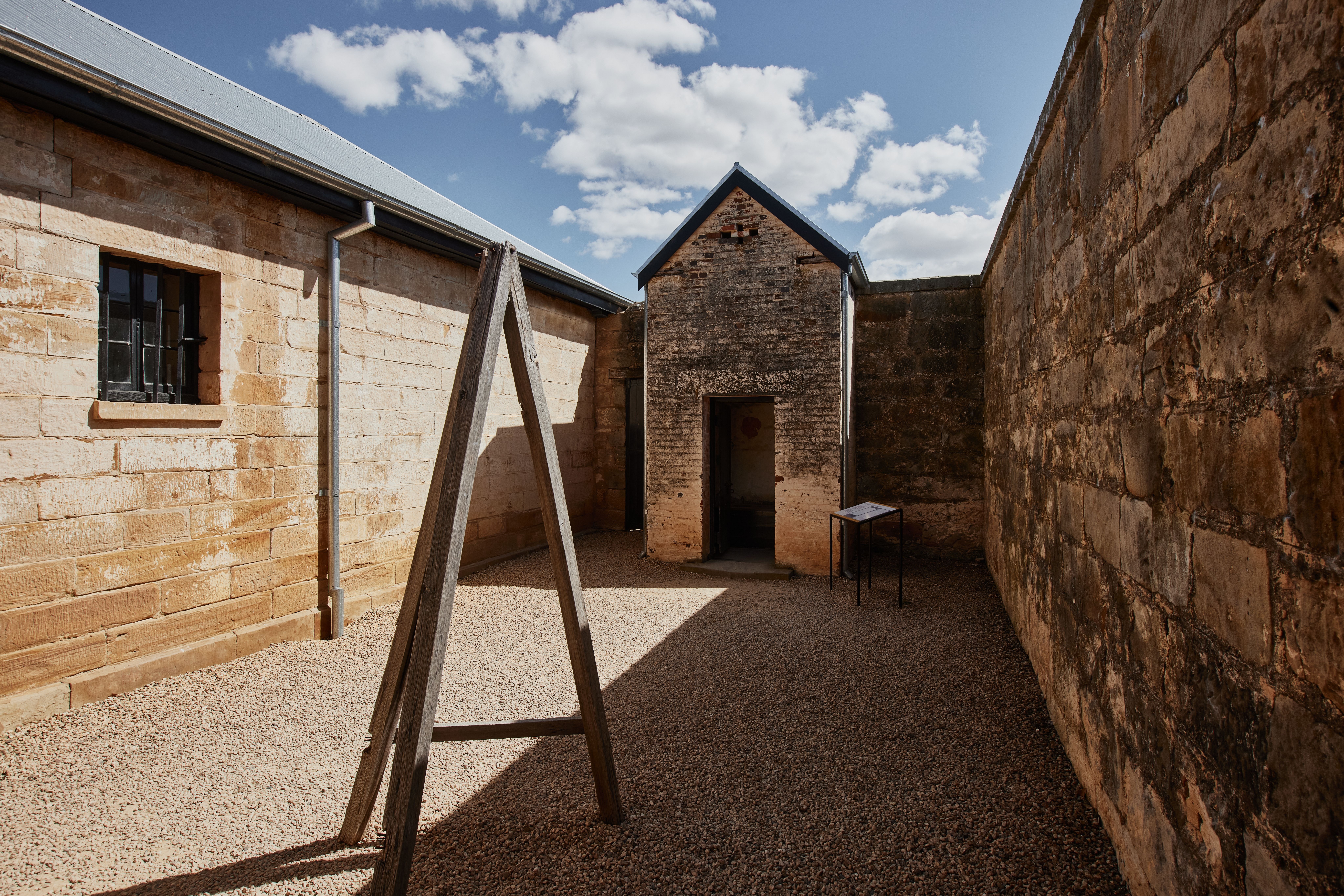 Sandstone walled courtyard with a wooden A-frame structure at Richmond Gaol, Richmond, Tasmania