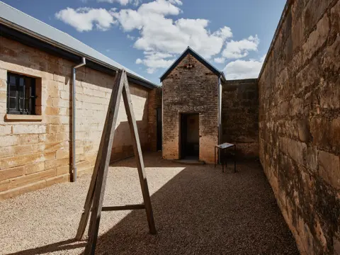 Sandstone walled courtyard with a wooden A-frame structure at Richmond Gaol, Richmond, Tasmania