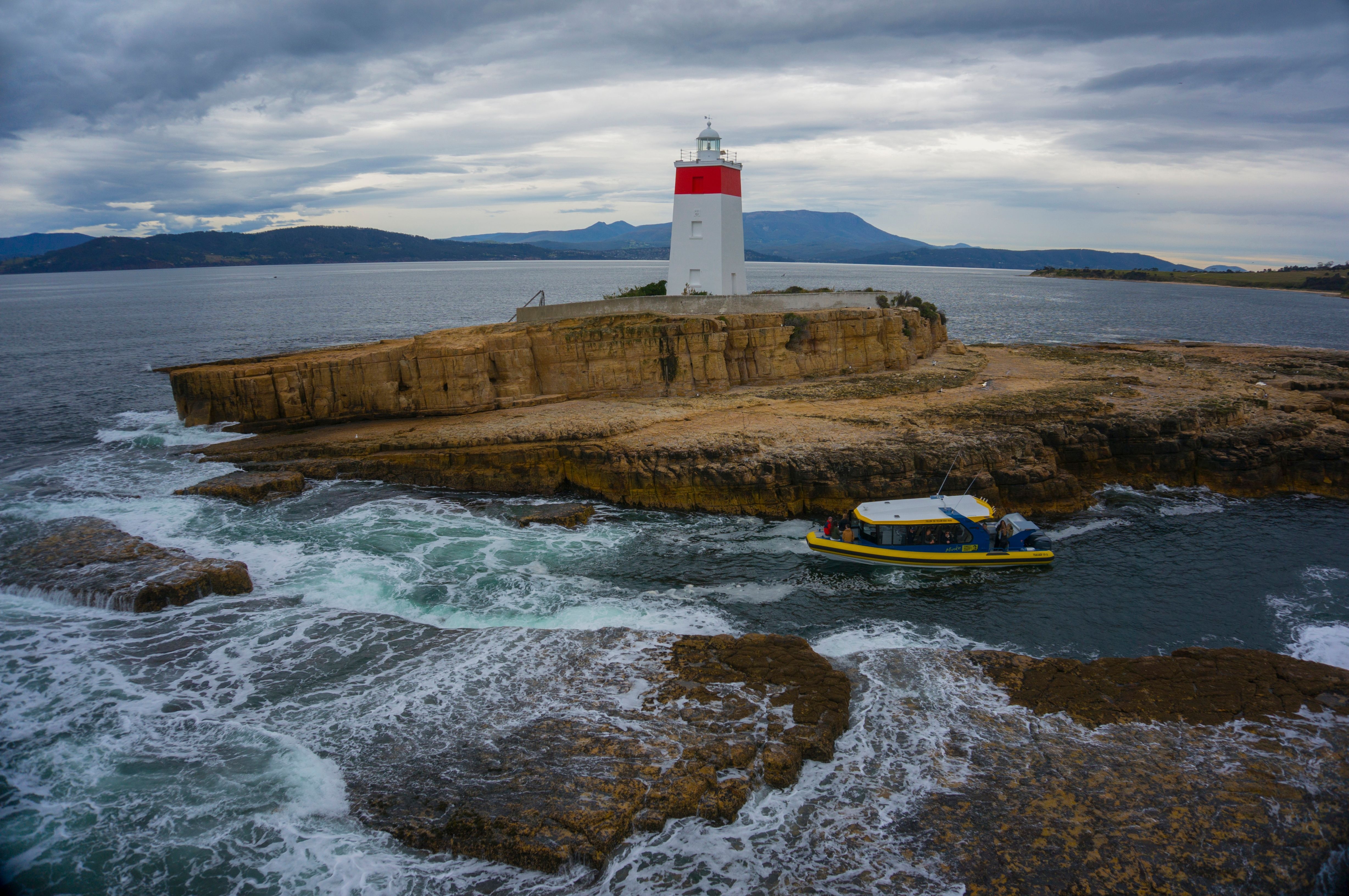Aerial view of an Iron Pot Cruises boat passing the Iron Pot lighthouse on a rocky island, Pennicott Wilderness Journeys, Tasmania