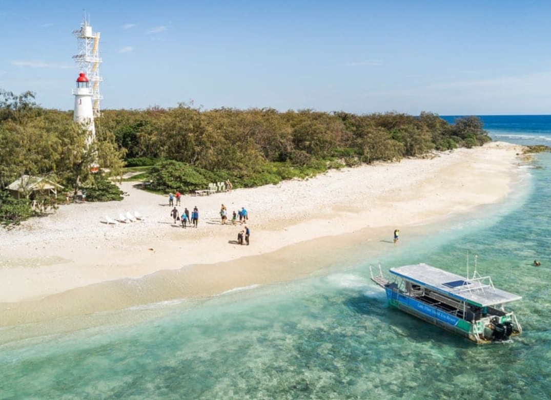 Aerial view of a tour group on the beach near a lighthouse with a boat moored in turquoise water, Lady Elliot Island