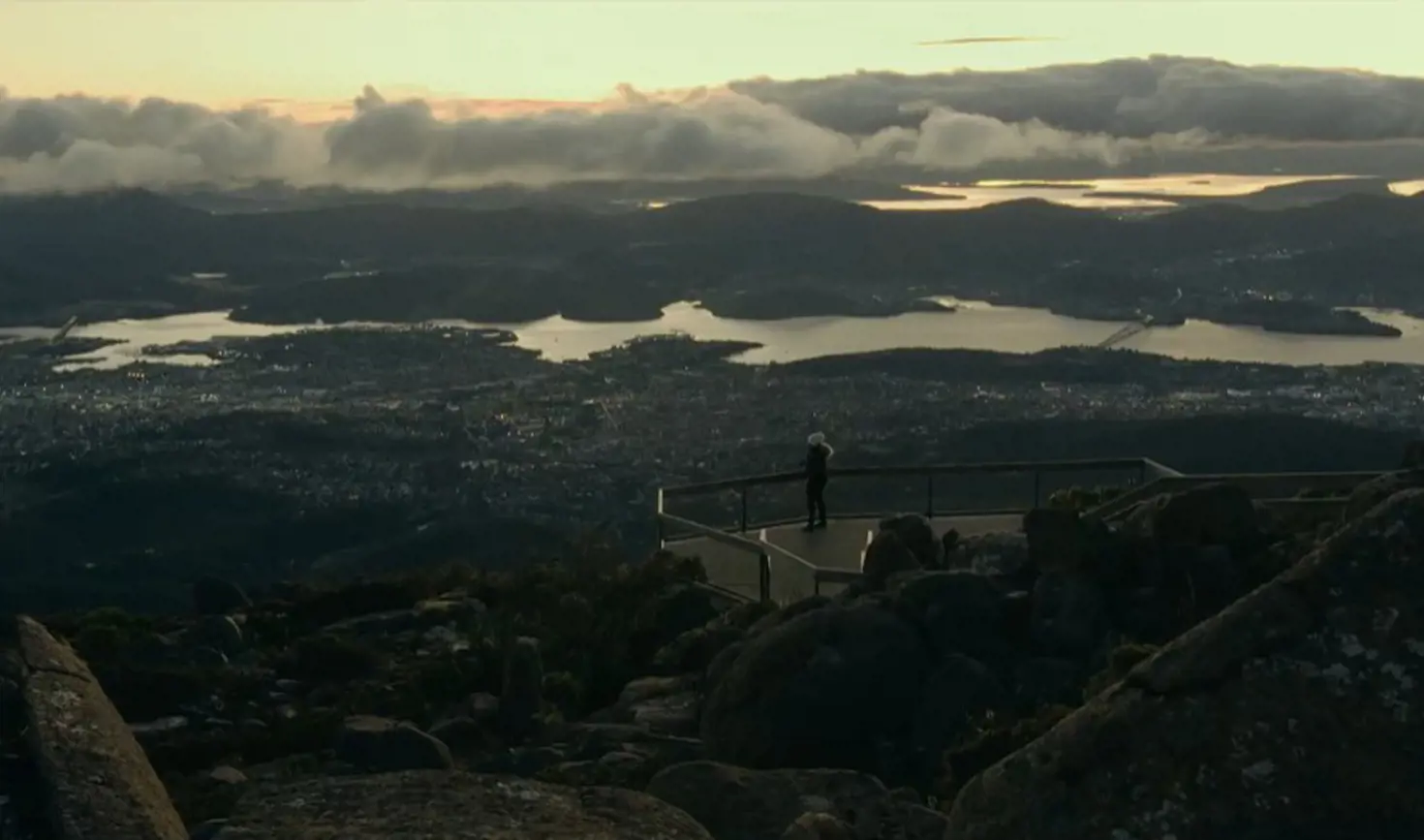 A person at the lookout on kunanyi / Mount Wellington overlooking Hobart and the Derwent in golden light, Tasmania