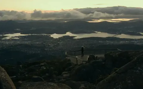 A person at the lookout on kunanyi / Mount Wellington overlooking Hobart and the Derwent in golden light, Tasmania