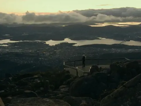 A person at the lookout on kunanyi / Mount Wellington overlooking Hobart and the Derwent in golden light, Tasmania