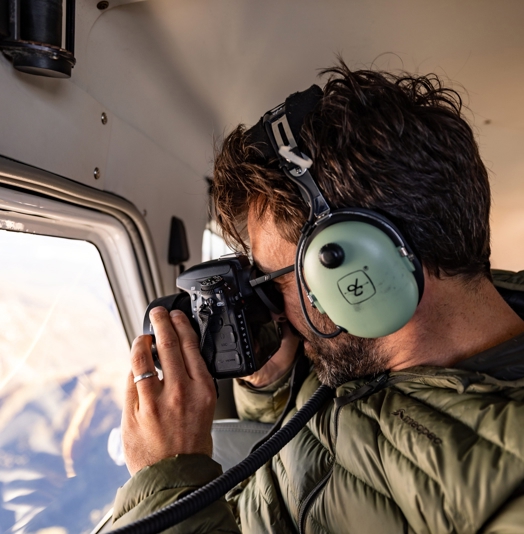 A person with aviation headphones photographing through a seaplane window on an Above and Beyond flight, Hobart, Tasmania