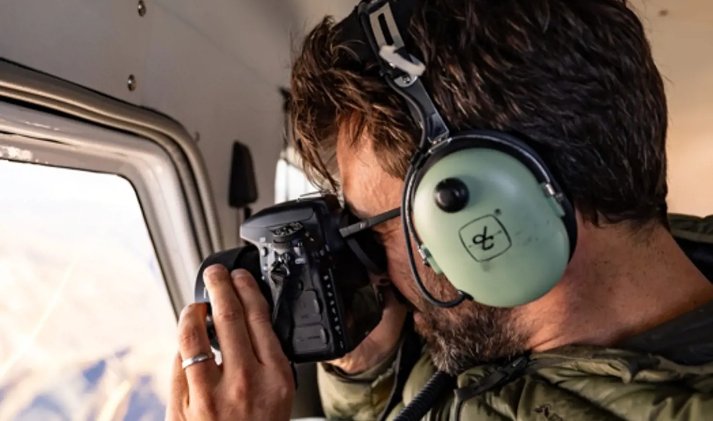 A person with aviation headphones photographing through a seaplane window on an Above and Beyond flight, Hobart, Tasmania