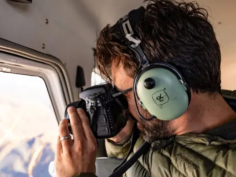 A person with aviation headphones photographing through a seaplane window on an Above and Beyond flight, Hobart, Tasmania