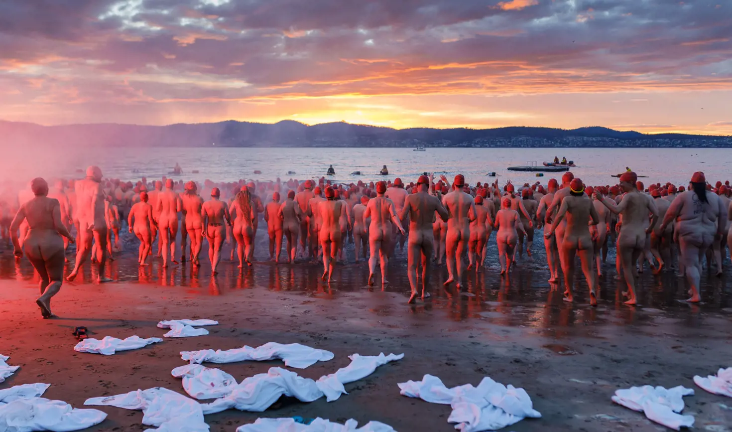 Swimmers running into the water in red caps at the Nude Solstice Swim during Dark Mofo, Long Beach, Sandy Bay, Tasmania